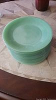 Stack of sixteen green jadeite dinner plates showing ribbed edge design.