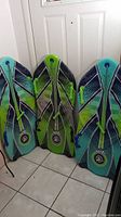 Three Sno-Storm Viper sleds with bright green and blue color scheme. All have four green handles attached. Minor wear visible. Sleds are shown upright against a door on tiled floor.