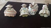 Overview of all four Lefton Bloomer Girl porcelain figurines arranged in a row on black surface.