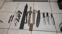 All knives arranged side by side on floor showing folding and fixed blades with various handle styles and sizes.