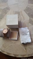 Michael Kors watch with box, instruction booklet, and original receipt neatly arranged on a marble surface.