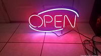 Front view of illuminated neon open sign showing red 'OPEN' text with white eye-shaped border on tiled floor.