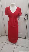 Red two-piece dress outfit with floral embroidery shown on mannequin in front of door