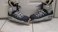 Side view of a pair of black and grey Roces Fifth Element inline skates on tile floor, showing size 13 and minor scuffs.