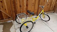 Full side and front angle of yellow tricycle leaning against wooden fence