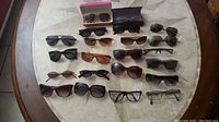 Top-down view of 15 sunglasses and eyeglass frames including Ray-Ban, various colors and styles