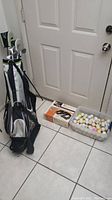 Photo showing golf bag, bucket of golf balls, and vintage chip and putt game box on the floor.