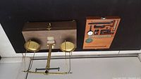 Vintage F. Hopken & Son brass balance scale with two pans on a central beam, mounted on a wooden base with case behind