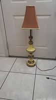 Full image of the lamp showing the fabric shade, brass and cream porcelain body, cord, and pull chain switch.