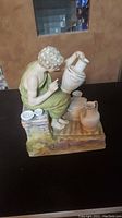 Porcelain Sylvan figurine of a lady potter shaping a vase, with multiple pots around her, on a detailed base.