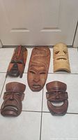 Five wooden hanging masks arranged on floor showing variety of sizes and expressions