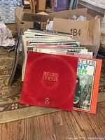 Photo of a group of vinyl albums including Bee Gees Odessa in red velvet sleeve plus other assorted albums arranged on floor and partially inside boxes
