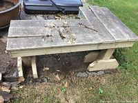 Wooden L-shaped bench from a front-side angle showing the rough wooden planks, L design, and some exposed nails.