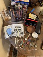 View of jewelry, watches, sunglasses with cases, makeup brushes with holder, skincare masks, and small wooden bowl on table.