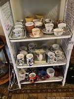 Shelf display of various mugs and china cups including floral and novelty patterns on a white wicker shelf