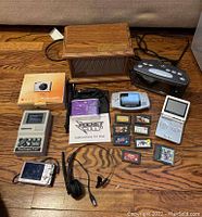 Lot contents arranged on floor showing all items described including air heater, cameras, game consoles, games, clock radio, power bank, and headset.