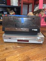 BSR McDonald 260 AX turntable sitting on top of JVC RX-DV31SL home theater receiver on wood floor. Turntable has a cracked dust cover with visible cracks reinforced by blue tape.