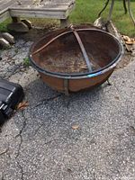 Full view of round metal fire pit on asphalt surface showing rust and weathering.