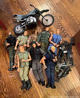 Top view of 8 G.I. Joe action dolls laid on wooden floor with a toy motorcycle beside them.