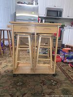 Front view of wooden kitchen island with 2 bar stools stored inside, showing drawers and wheels.