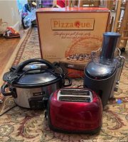 Photo showing the Crockpot, red toaster, juice extractor, and boxed Pizza Que pizza stone together on carpeted floor.