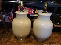 Two ceramic lamps sitting on the floor without lampshades, one lamp appears slightly lighter in color