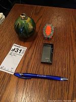 Top view of all three lighters placed on a wooden surface with a blue pen and auction lot card for scale.