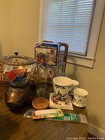 Full view of assorted items on table including woven baskets, herb garden kit, glass propagation station, ceramic pots, wooden fish stand, and vintage matchbox collection.
