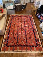 Full view of the woven Southwestern style rug laid out showing red main field with geometric desert motifs and blue inner border.