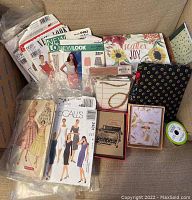 Lot items on beige carpet including sewing patterns, stationery boxes, ribbon, and Vera Bradley frame.