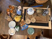 Full overhead view of all items on wooden surface including chalk tray, metal and copper glasses, nutcrackers, teapot set, bunny coasters, honey pot, meat choppers, and folding server.