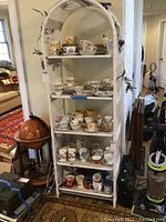 Front view of white wicker shelf unit with multiple shelves displaying decorative teacups and saucers.