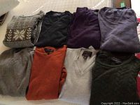 Photo showing all seven folded men's cashmere sweaters in an assortment of colors and patterns.