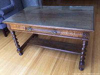 Full view of antique oak table with glass top protector showing the barley twist legs and drawer front.