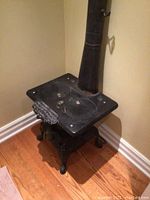 Full view of the antique black cast iron wood stove against a wall, showing the flat cooking surface with two burner plates and attached vent pipe.