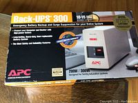 Front view of the APC Back-UPS 300 box showing the battery backup and surge suppression unit with details of 10-15 minutes runtime, 200W/300VA power.