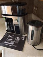 Braun coffee maker plus, Breville electric kettle and user manual displayed on counter, showing full set.