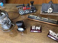 Top view of all railroad collectibles arranged on wooden table including cast iron steam locomotive, miniature train replicas, converted lantern and doorstop.