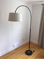 Full view of the black floor lamp with curved arm, white fabric lampshade, and black marble base, showing height and structure.
