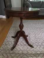 Full view of the cherry wood circular table showing the round top, pedestal base, and legs with brass foot caps.