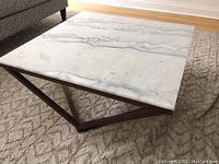Full view of the square marble top showing natural gray veining and smooth polished finish, resting on the geometric wooden base.