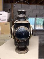 Front view showing blue glass lens on black metal lantern body with rust and wear.