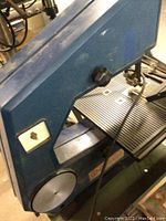 Bandsaw side view showing blue textured metal body, power switch, and round lower wheel.