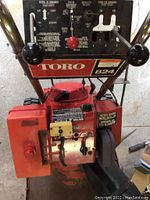 Front view of Toro 824 snowblower showing engine, controls with dual levers and red knob, branding and some rust on metal surfaces.