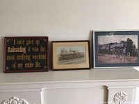 Two framed railroad photographs displayed on a wall, including a humorous railroad sign.