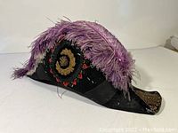 Side view of black beaver felt bicorne hat with bullion patch and purple feather trim
