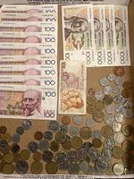 Photo showing several Belgian 100 Franc banknotes stacked alongside various foreign coins in silver and bronze tones.