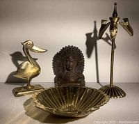 Four brass desk items: pelican photo holder, Native American bookend, ornate candleholder bookend, and small brass bowl.