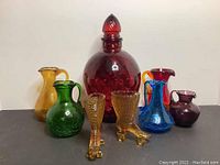 Front view of the set showing the large red decanter in the back center, surrounded by small pitchers in amber, green, red, blue, purple and two amber roller skate figurines in front.