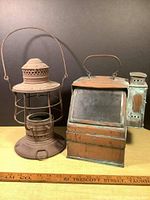Front and side view of two antique lanterns side by side on a dark background with ruler for scale.